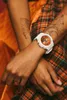 A close-up shot of a person's arms wearing a white watch with a copper face, set against a plaid background. Anteprima dell’immagine prodotto