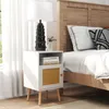 A white nightstand with a woven cane door is placed next to a bed with wooden headboard. Náhled obrázku produktu