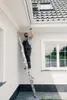 A man is on a ladder inspecting the exterior of a house. Podgląd zdjęcia produktu