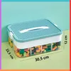 A clear, well-lit image of a two-tiered storage container filled with colorful building blocks, placed on a light green surface against a light blue background. Dimensions are indicated with lines and text. Produktbild-Vorschau