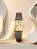A gold-toned rectangular watch with a gray leather strap is displayed against a soft, abstract background with flowing curves. Podgląd zdjęcia produktu
