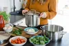 A person is preparing food in a kitchen, with various ingredients and cooking pots on the counter. Produktbild-Vorschau