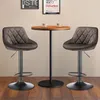 Two brown velvet bar stools are placed around a small round wooden table with two white cups on it, in a room with framed pictures on the wall. Voir les images du produit