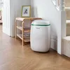 A white dehumidifier with a green stripe is placed on a wooden floor next to a staircase and a wooden shelf with books. Náhľad obrázku produktu