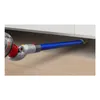 A close-up view of a vacuum cleaner attachment being used to clean a narrow space between a cabinet and the floor. Podgląd zdjęcia produktu