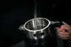 A hand is holding a black and silver electric kettle while water is being poured into it from a faucet. Podgląd zdjęcia produktu