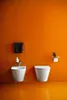 A modern bathroom with an orange wall and floor, featuring a white toilet and bidet. Produktbild-Vorschau