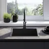 A modern kitchen sink with a black faucet, set against a window with a view of greenery. Náhled obrázku produktu