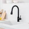 A black kitchen faucet is shown above a white sink, with kitchen utensils and a lemon on the counter. Produktbild-Vorschau