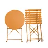 A round orange bistro table and stacked chairs. Produktbild-Vorschau
