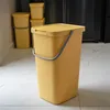 A yellow trash can with a lid and handle sits on a tiled floor in a kitchen setting. Podgląd zdjęcia produktu