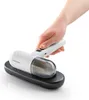 A hand holding a white and gray handheld vacuum cleaner on its charging base. Voir les images du produit