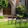 Several black folding chairs are set up on a grassy lawn in front of a large building with an arched entrance. Podgląd zdjęcia produktu
