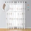 A pair of sheer curtains with a leaf embroidery pattern hanging in front of a window. Produktbild-Vorschau