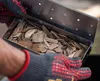 Hands wearing grilling gloves holding a smoking box filled with wood chips. Produktbild-Vorschau