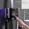 A hand is shown using an electric toothbrush with a toothpaste dispenser and toothbrush holder mounted on a wall. Náhled obrázku produktu