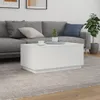 A white coffee table is placed in front of a gray sofa in a living room setting. A plant is visible to the right of the sofa. Náhled obrázku produktu