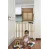 A baby is playing with toys in front of a wooden baby gate in a kitchen. Podgląd zdjęcia produktu
