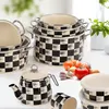 A collection of black and white checkered cookware, including pots, a teapot, and storage containers, arranged on a white surface with some vegetables in the background. Náhled obrázku produktu