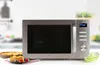 A microwave oven is shown on a countertop with a pie and a slice of cake in front of it. Náhled obrázku produktu