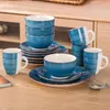 A set of blue and white ceramic dishes and mugs are arranged on a wooden table. Náhled obrázku produktu