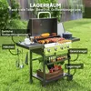 A gas grill is set up on a grassy lawn, with various food items cooking on the grill and vegetables in a crate below. The image highlights different features of the grill with text labels. Náhled obrázku produktu