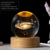 A 3D crystal ball with a galaxy engraving, illuminated by warm light, resting on a wooden base. An astronaut figurine is partially visible on the right. Produktbild-Vorschau
