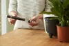 A person is holding a plant watering device next to two potted plants. Produktbild-Vorschau