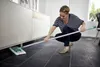 A woman is cleaning the floor under a cabinet with a mop. Produktbild-Vorschau