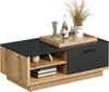 A modern coffee table with a black top and wooden base, featuring a drawer and open shelving. It is styled with decorative items like a decanter, wine glasses, a bottle, and dried grass in a vase. Voir les images du produit
