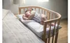 A baby sleeping in a crib attached to a bed. Produktbild-Vorschau