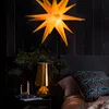 A bedroom scene with a star-shaped lamp, a bedside table with a lamp and candles, and a pillow on the bed. Produktbild-Vorschau