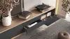A modern TV stand with an open drawer and a turntable on top, placed in a living room setting with a rug and decorative vase. Náhled obrázku produktu