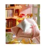 A close-up of a miniature pink armchair with a white and gray pillow on it, placed in a dollhouse setting with bookshelves in the background. Anteprima dell’immagine prodotto