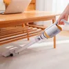 Weißer und oranger Handstaubsauger wird verwendet, um unter einem Holztisch auf einem hellen Teppich zu reinigen Produktbild-Vorschau