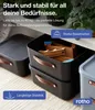 Two black storage boxes are stacked on top of each other, with a gray storage box to the right. The boxes contain wooden toys. The background is a shelf with plants. Produktbild-Vorschau