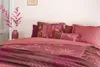 A bed with pink bedding and decorative pillows, with a vase of pink flowers on the left. Produktbild-Vorschau