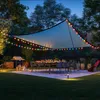 An outdoor patio scene at dusk, set up for a gathering with a dining table, chairs, and a grill, illuminated by string lights. Produktbild-Vorschau