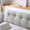 A large, tufted wedge pillow is placed on a bed with a checkered sheet. A laptop is visible on the bed in front of the pillow. Produktbild-Vorschau