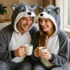 A couple wearing husky-themed onesies are sitting on a couch, holding mugs of hot beverages and smiling at each other. Anteprima dell’immagine prodotto