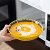 A hand holding a bowl of soup in front of a microwave. Produktbild-Vorschau