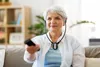 An elderly woman is sitting on a couch and watching TV. Produktbild-Vorschau