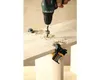 A hand is using a drill to make a hole in a wooden board. There are wood shavings around the hole. Two corner clamps are attached to the board. Produktbild-Vorschau
