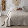 A bed with a beige quilted bedspread and decorative pillows. Produktbild-Vorschau