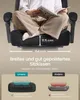 A person sitting cross-legged on a black gaming chair, holding a magazine. The image includes diagrams and text highlighting the chair's seat cushion dimensions and comfort. Produktbild-Vorschau