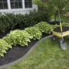 A garden bed with black mulch, hosta plants, and a wheelbarrow with a shovel. Produktbild-Vorschau