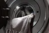 A close-up view of a washing machine drum with a towel being loaded. Produktbild-Vorschau