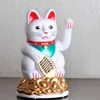 A white Maneki-neko (lucky cat) figurine with red ears and collar, holding a gold coin, sits on a base of gold coins against a textured light gray and white background. Produktbild-Vorschau