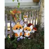 Three plush foxes of different sizes are arranged in an outdoor setting with a wooden fence, grass, mushrooms, and pinecones. Produktbild-Vorschau