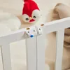 A close-up view of a white wooden crib railing with a safety latch and a red stuffed toy in the background. Náhľad obrázku produktu